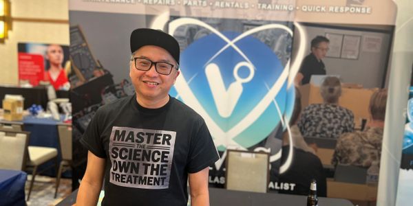 Smiling man in glasses and cap at a science-themed booth with promotional items.