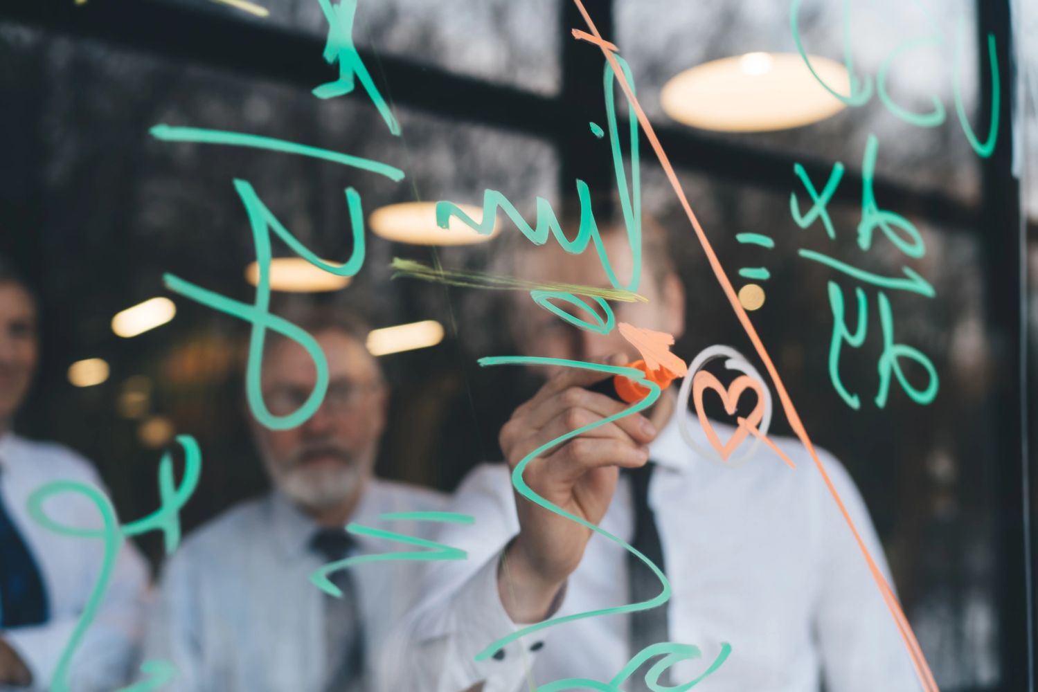 Through glass of confident coworkers using marker while taking notes