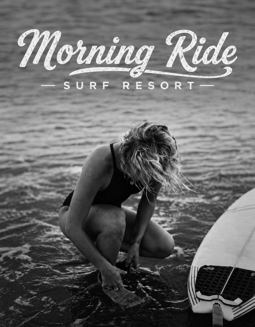 Woman in swimsuit preparing surfboard in water at a surf resort.
