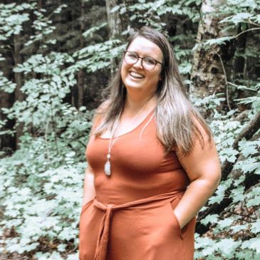 Smiling woman in a rust-colored outfit in a wooded area.