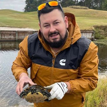 Man holding a turtle near a pond.