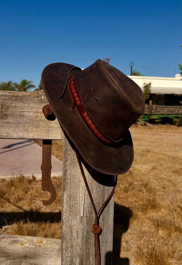 Brown leather cowboy hat on wooden post.