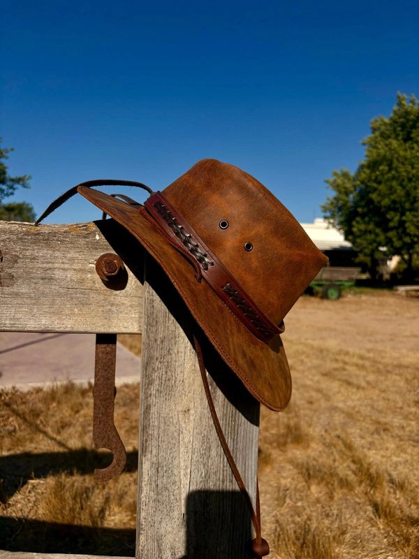Brown leather cowboy hat on wooden post.