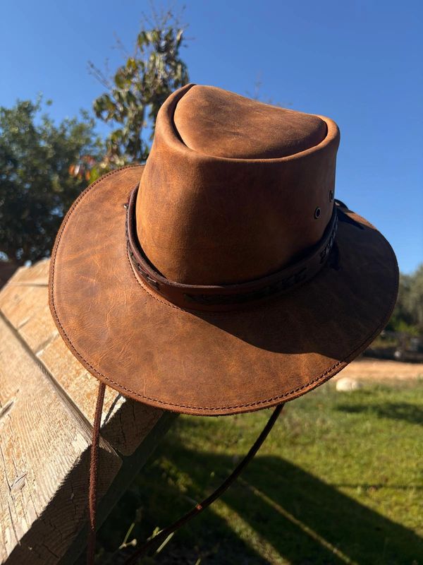 Brown leather cowboy hat on a wooden fence.
