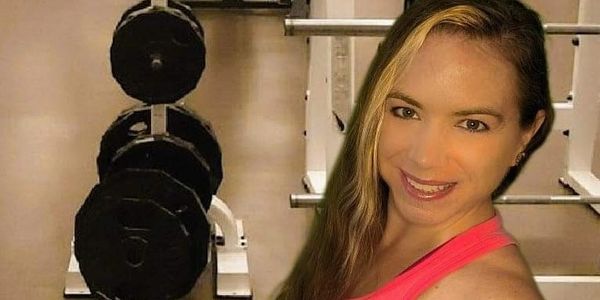 Woman in pink top smiling in gym near dumbbells, conveying strength and positivity.