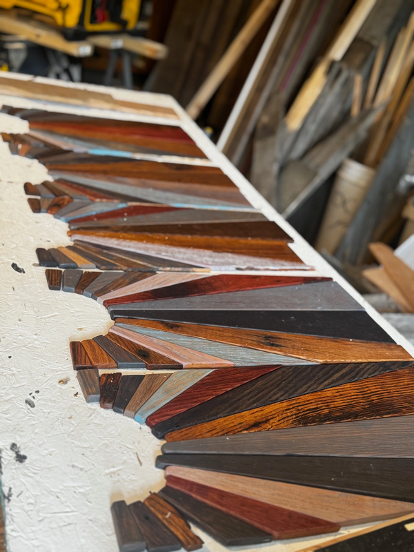 Stained barnwood pieces arranged in a geometric sun pattern on a workbench in a woodworking studio