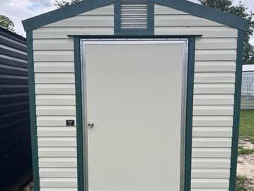 Small white storage shed with green trim and closed door.