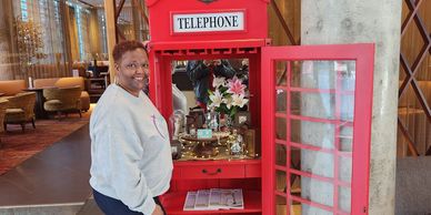 Woman smiling beside an open red telephone booth repurposed as a decorative display.