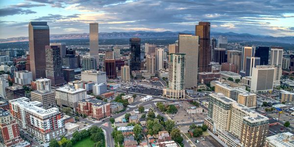 Aerial view of a modern city skyline with tall buildings and mountains in the background.