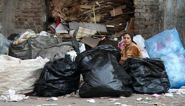 A woman sorting through large bags of trash on the ground
