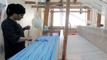 A woman cutting colored string next to a manual loom