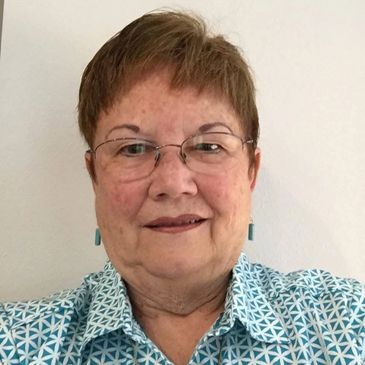 Portrait of a smiling elderly woman wearing glasses and a patterned blue shirt.