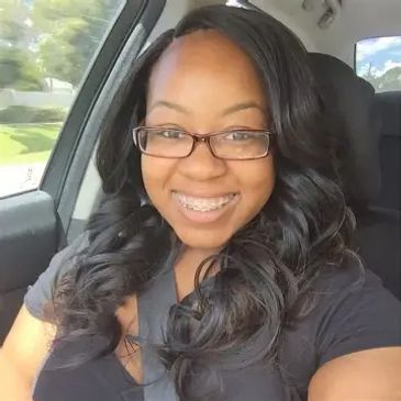 Smiling woman with glasses and long curly hair inside a car.