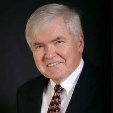 Smiling elderly man in a suit and tie against a dark background.