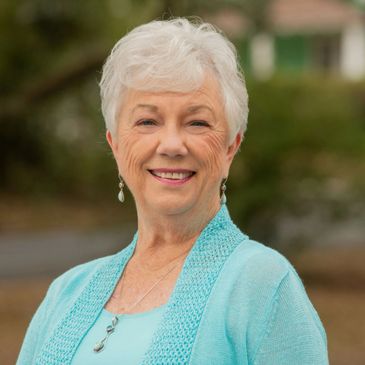 Smiling elderly woman wearing a light blue top and cardigan outdoors.