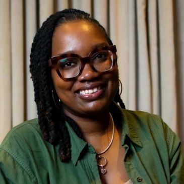 Smiling woman with glasses and braided hair in green shirt.