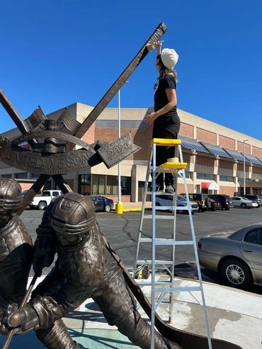 Applying cold wax to 'The Pride of Saginaw' sculpture by Steven Hargash, in Saginaw.