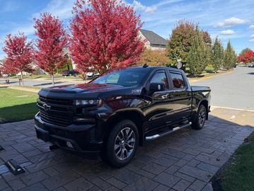 Black Chevrolet pickup truck parked on a driveway with autumn trees in the background.