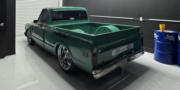 Green vintage GMC pickup truck with shiny rims in a garage.