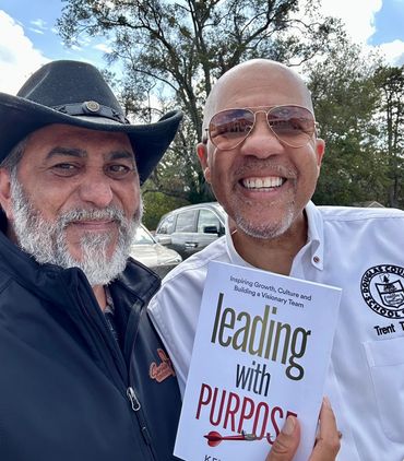 Two men smiling, one holding a book titled 'Leading with Purpose'.