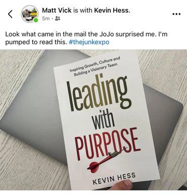 A book titled 'Leading with Purpose' by Kevin Hess held over a laptop.