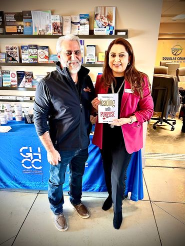 Two people smiling, one holding a book titled 'Leading with Purpose' at a Georgia Hispanic Chamber of Commerce event.