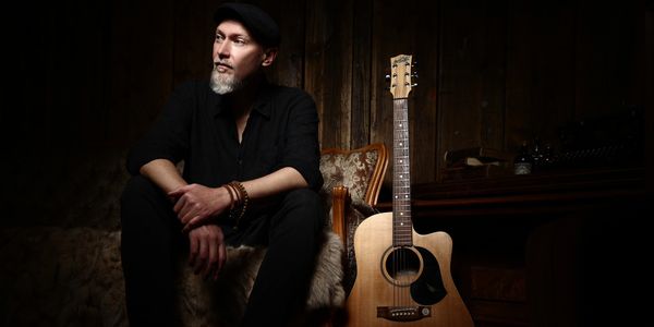 Marcus Schultz von der Firma Manda Records in Berlin sitzt auf einem Sofa mit einer Akustikgitarre