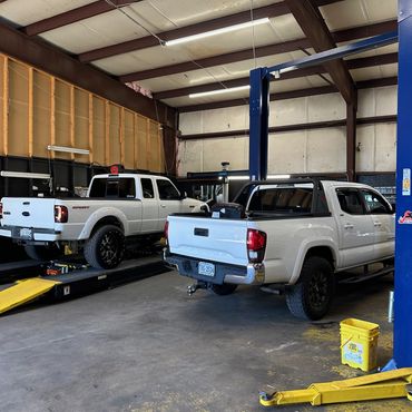 Two white pickup trucks inside a spacious auto repair shop.
