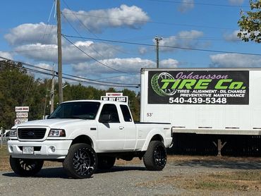 White Ford pickup truck parked near a tire service trailer on a sunny day.