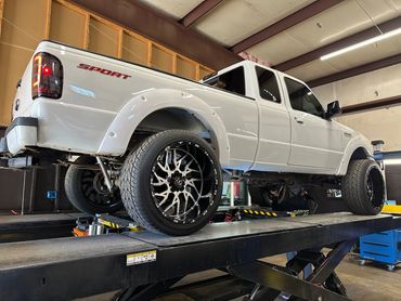 White lifted pickup truck on a garage lift with custom wheels.