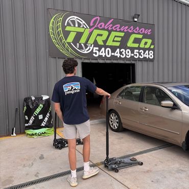 Person with a car jack outside Johansson Tire Co. shop.