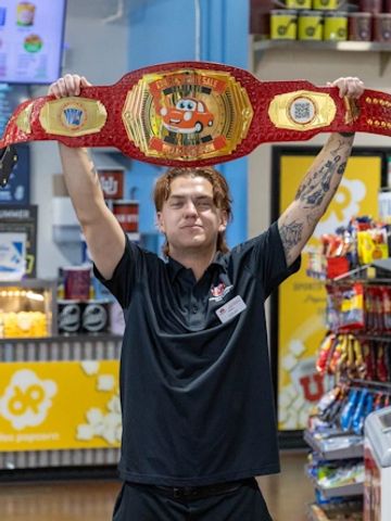 Person holding a large, colorful championship belt indoors.