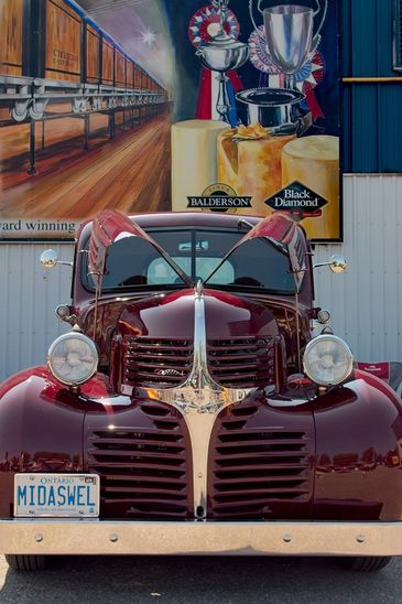 Front view of a shiny vintage car with gull-wing doors open, parked in front of a cheese-themed mural.