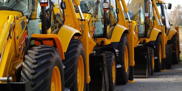 A row of yellow construction vehicles parked in a line outdoors.