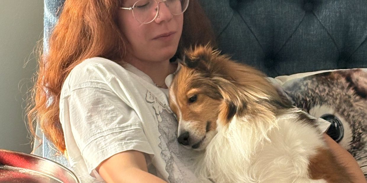 Person with red hair lovingly cuddles a fluffy dog on a couch.