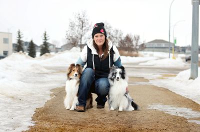 Woman crouching outdoors with two dogs on a snowy path.