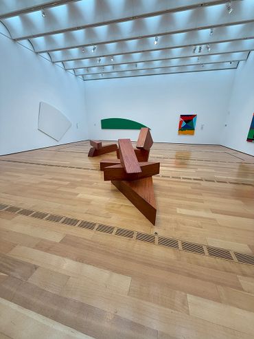 Modern art gallery with wooden sculpture and colorful abstract paintings on white walls.