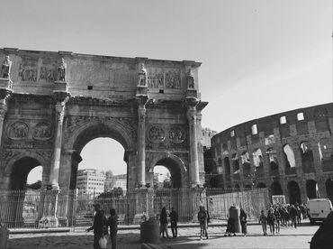 Black and white photo of the Arch of Constantine and Colosseum in Rome with tourists.