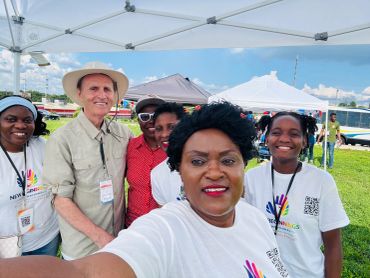 Group selfie at an outdoor event with smiles and tents.