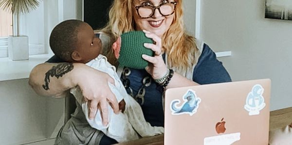 Female by laptop holding a green breast model and Black doll baby with various bottles and pump part