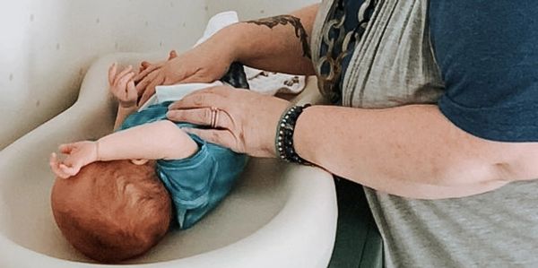 Woman with reddish hair changing a baby's diaper in a well lit room on a changing table