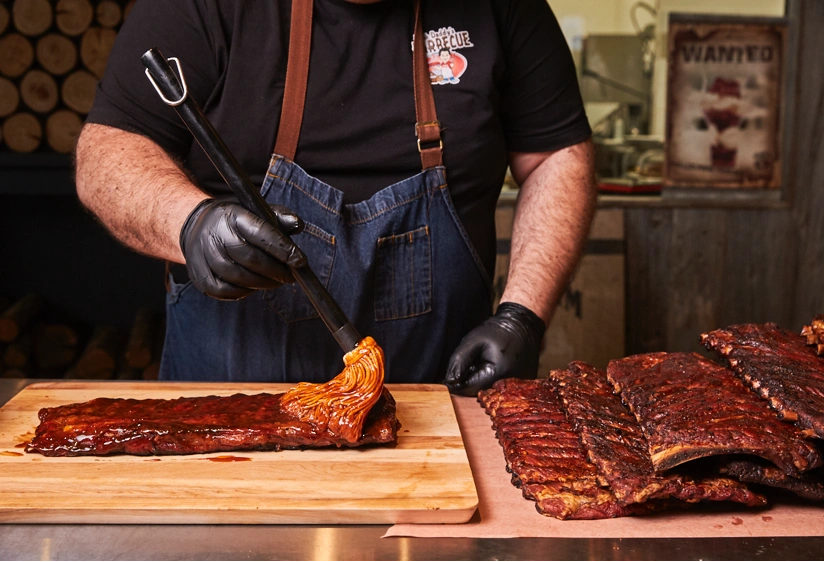 Pitmaster and owner Frank brushes his famous smoked St. Louis Style Ribs with housemade BBQ sauce