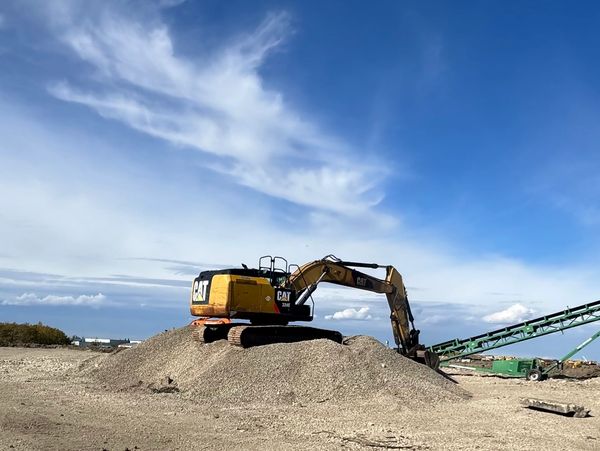 Excavator on gravel pile under blue sky.