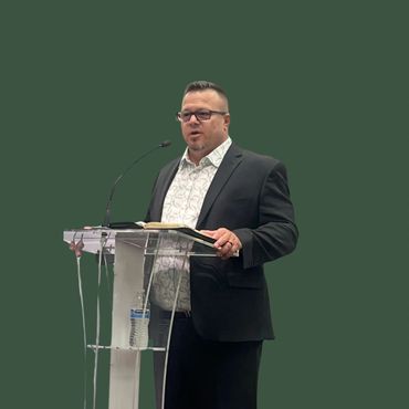 Man in suit speaking behind a clear podium with a microphone and a water bottle.