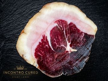 Close-up of a sliced cured meat on dark surface.