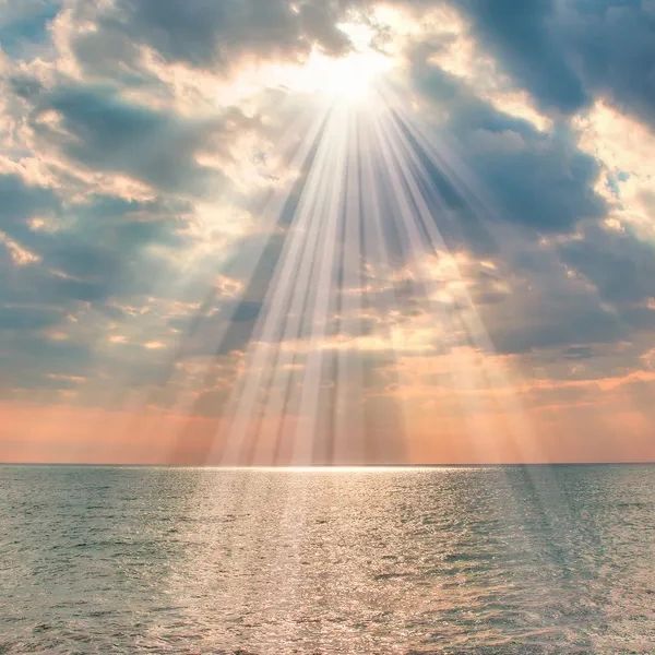 Sunlight rays break through clouds over a calm sea.