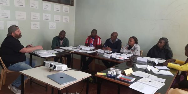 Group of people engaged in a meeting with documents and a projector on the tables.