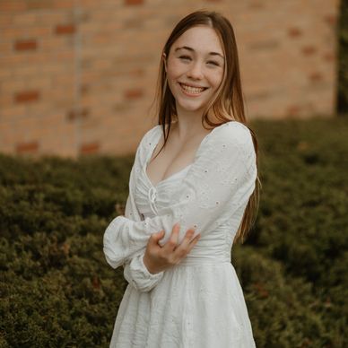 Young woman smiling warmly in a white dress outdoors.