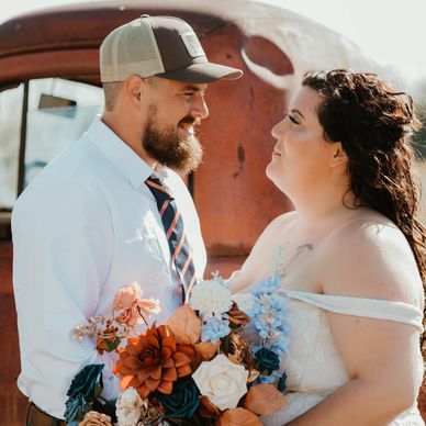 Couple sharing a tender moment with a vibrant bouquet and rustic backdrop.