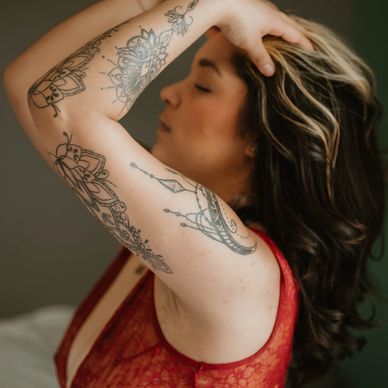 Woman in red lace with intricate arm tattoos poses with eyes closed.